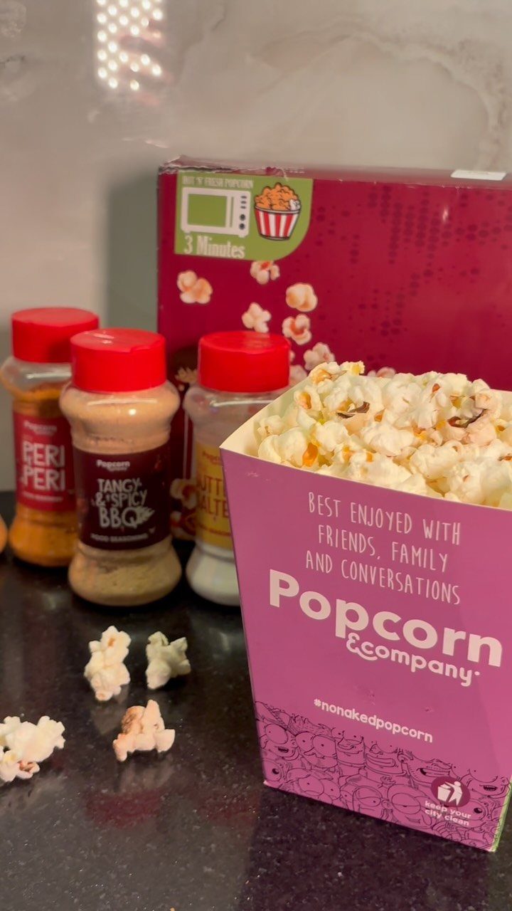 Popcorn seasoning shakers and a pink box of popped corn on a counter.