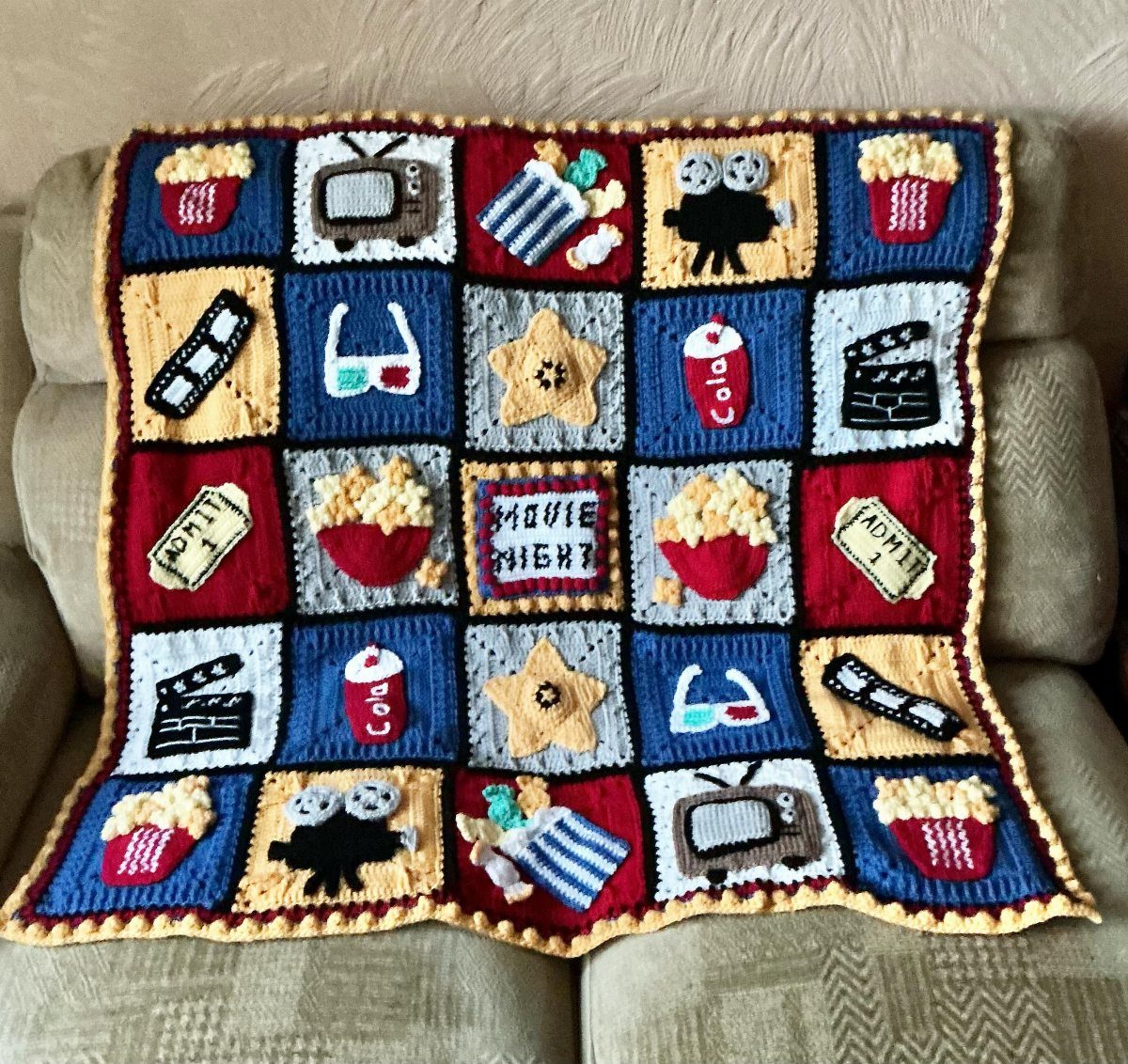 Crochet movie-themed blanket with popcorn and cinema icons draped over a beige sofa.