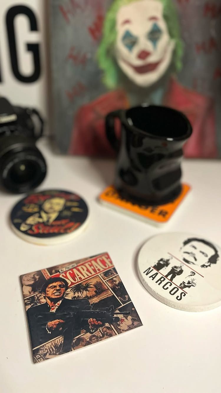 Movie-themed coasters with film characters and a black mug on a white surface.