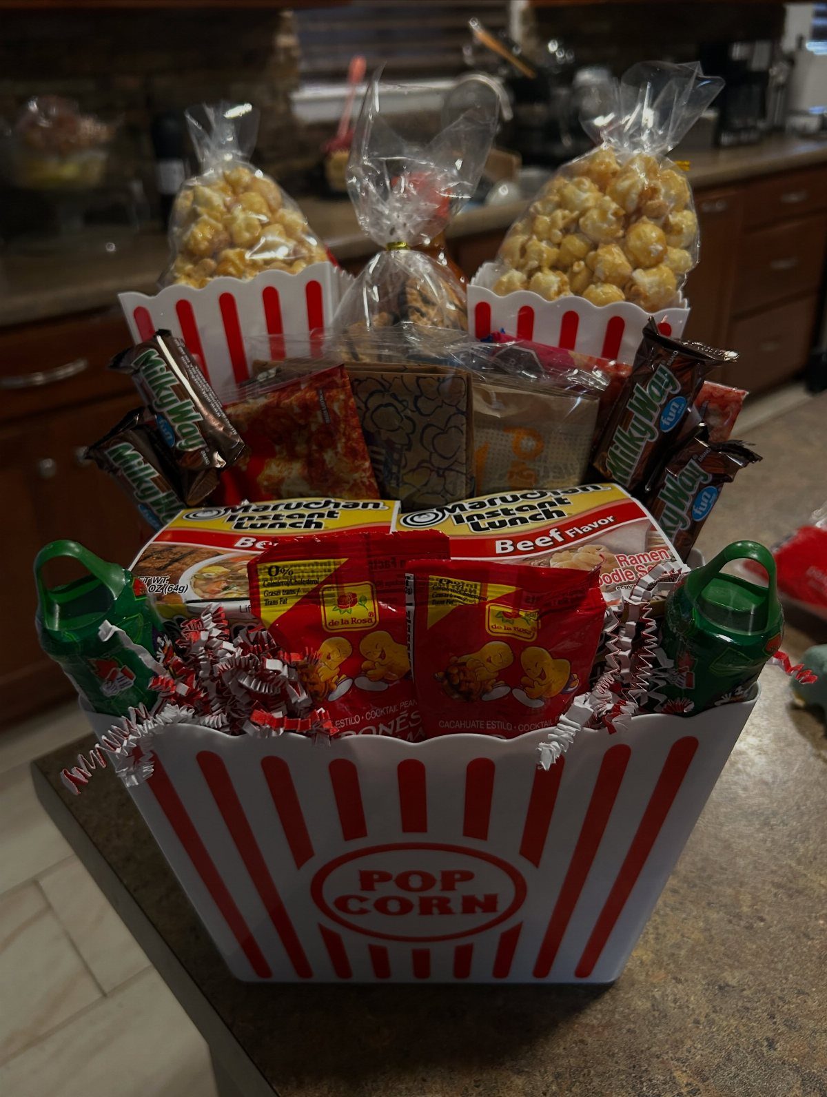Popcorn-shaped gift basket filled with popcorn, candy, and snacks on a counter.