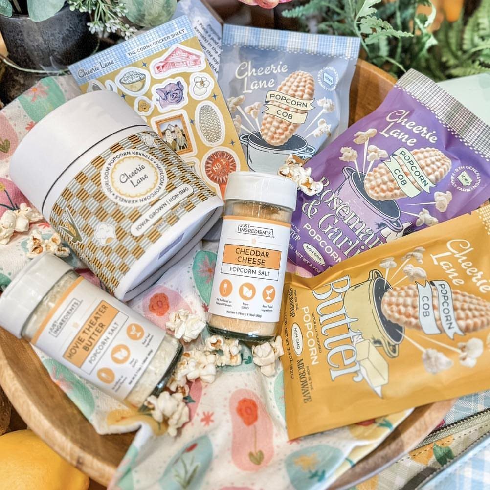Popcorn seasonings and kernels in a wooden tray with scattered popped corn.