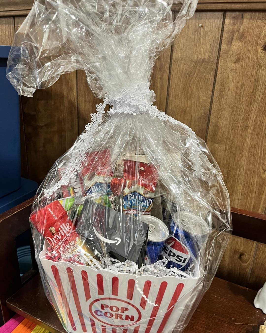 Movie night gift basket in a popcorn tub filled with candy and snacks.