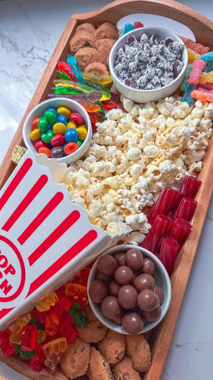 Wooden snack tray with popcorn, colorful candies, cookies, and a popcorn container.