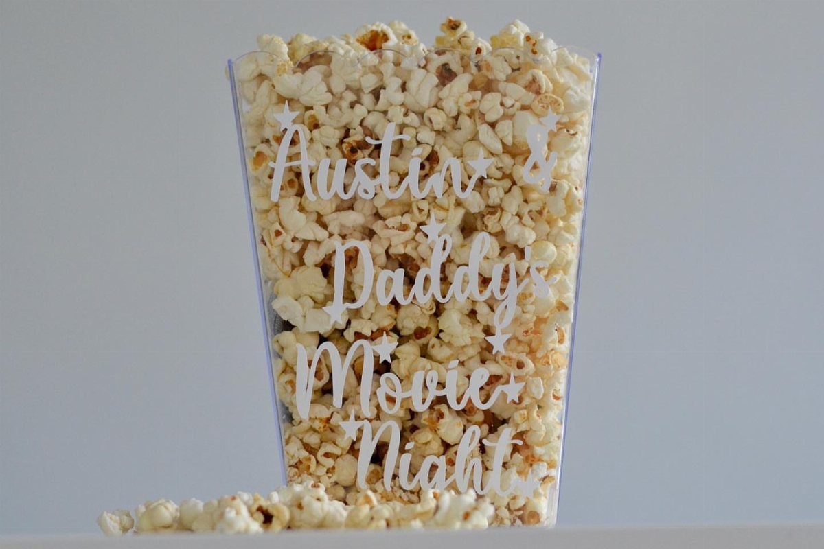 Clear plastic popcorn tub filled with popcorn and personalized movie night text.