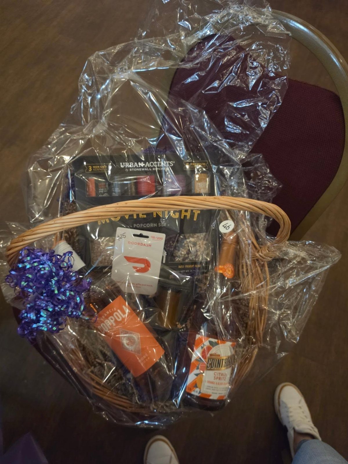Movie night gift basket wrapped in cellophane with snacks and a purple bow.