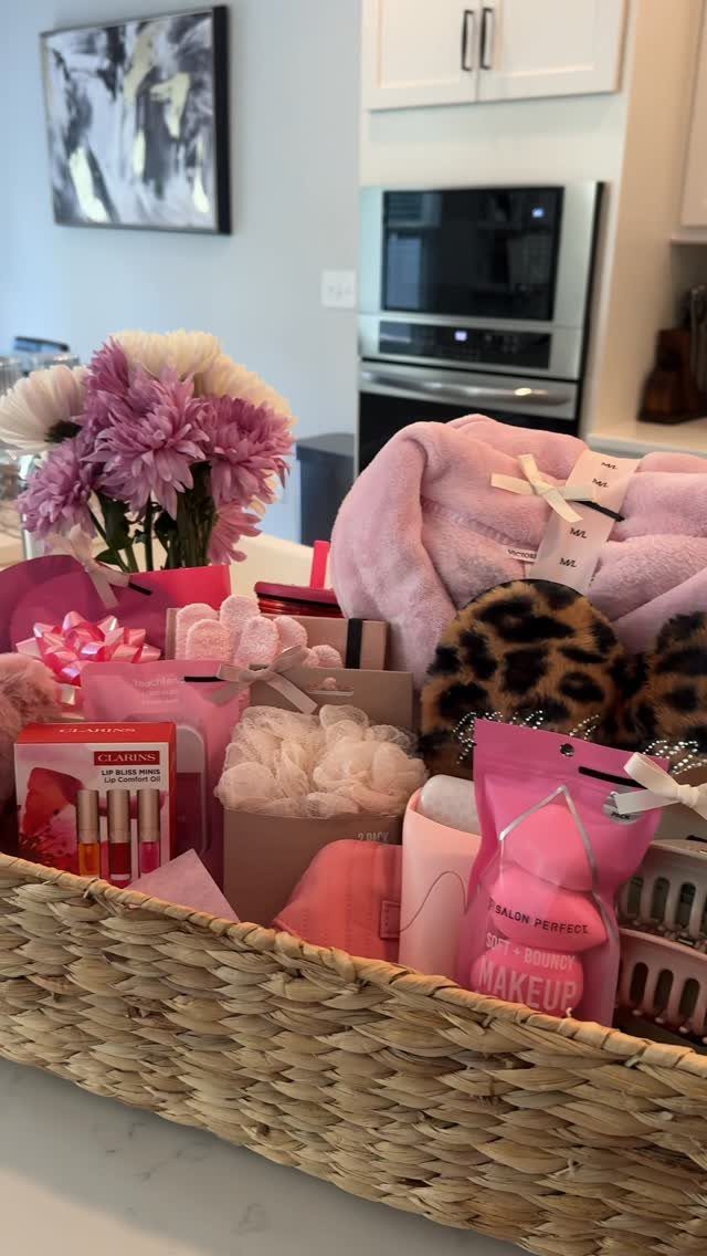 Woven gift basket filled with pink robe, leopard slippers, beauty products, and flowers.