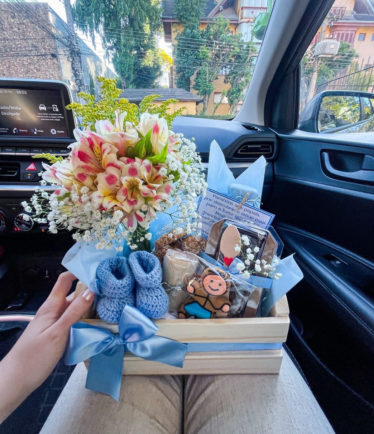 Gift basket with pink lilies, blue baby booties, and treats in a wooden crate.
