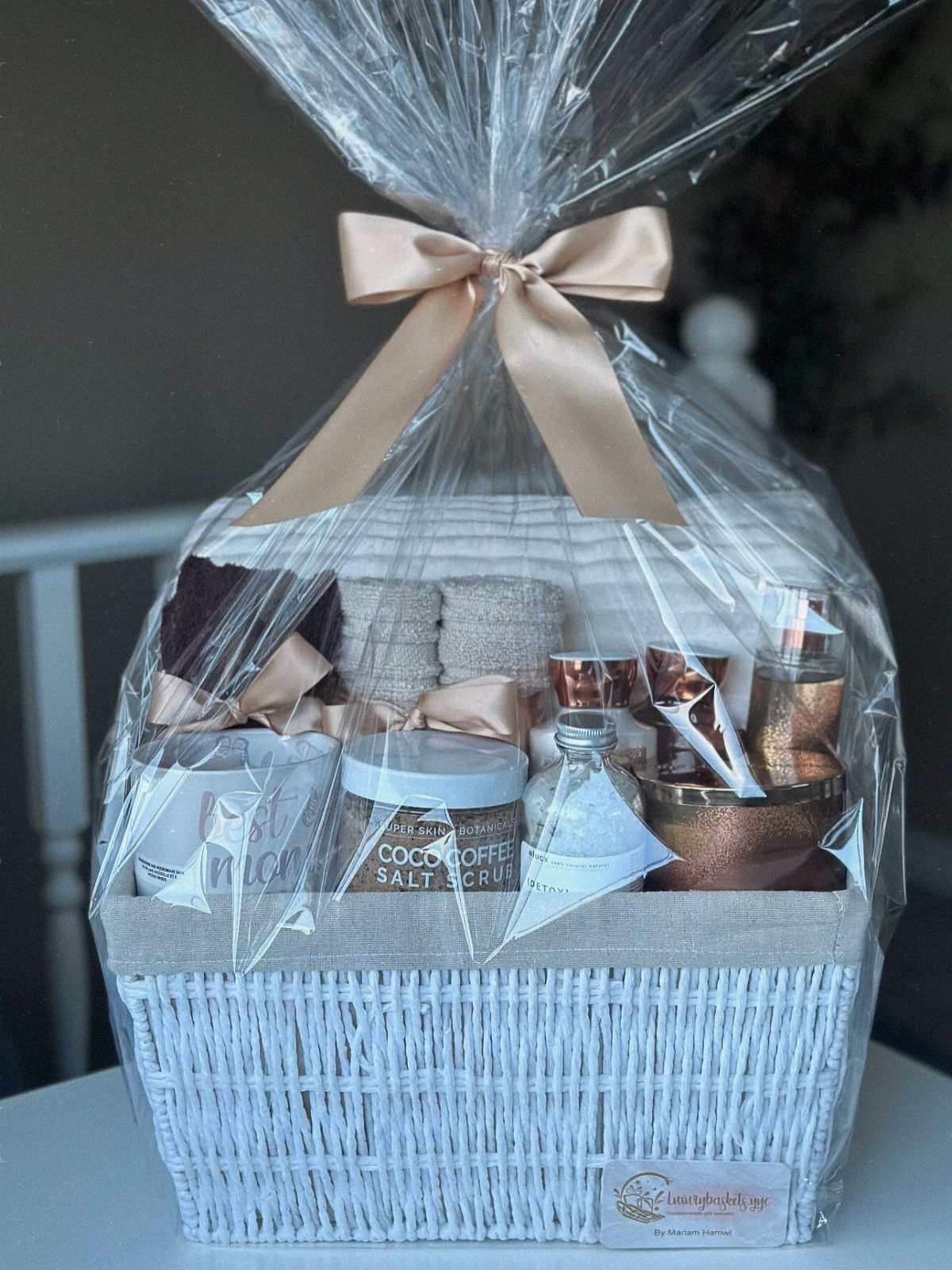 White wicker gift basket with spa products wrapped in clear cellophane and bow.