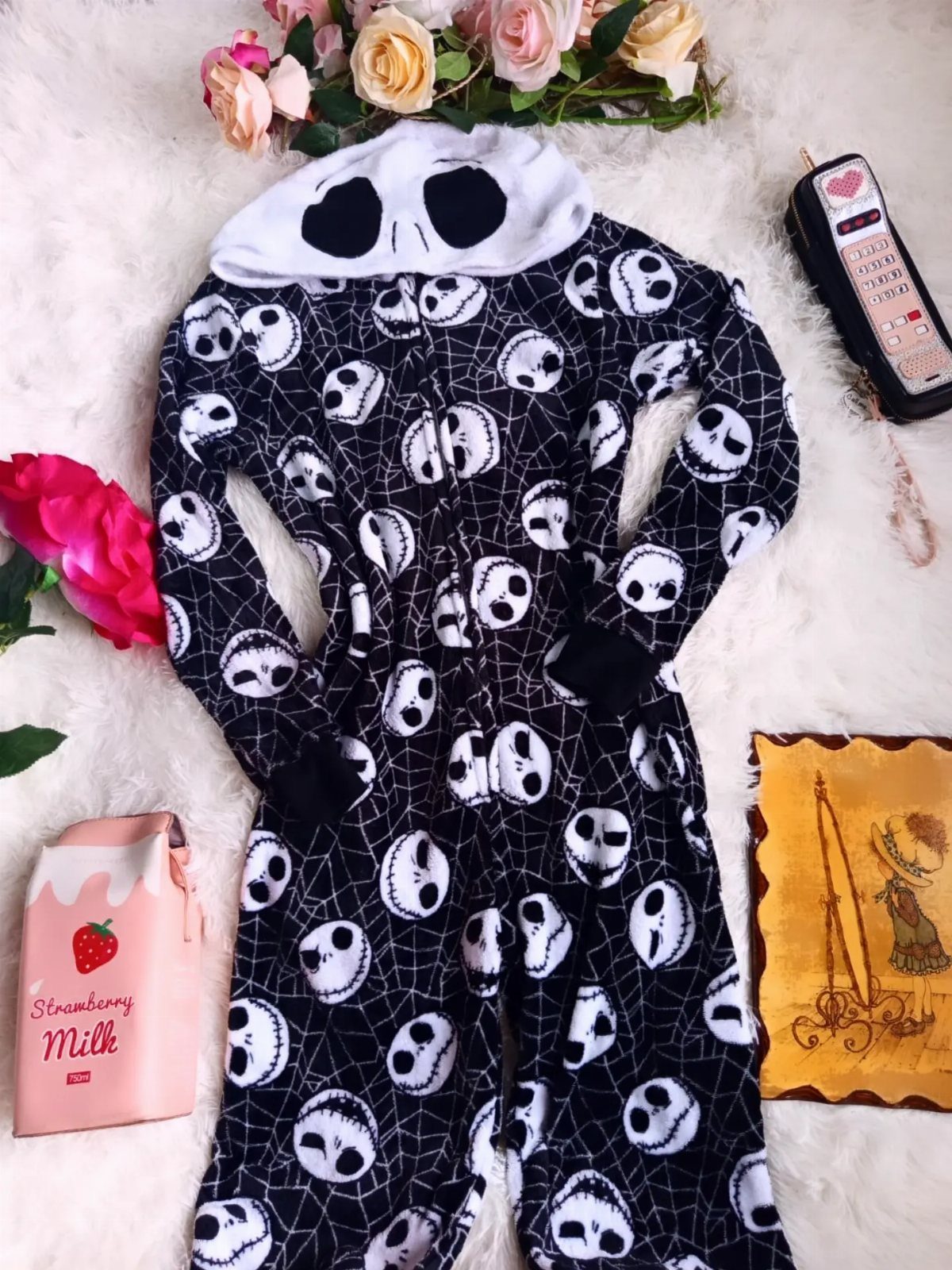 Jack Skellington patterned one-piece pajamas laid on a white fluffy rug with flowers.