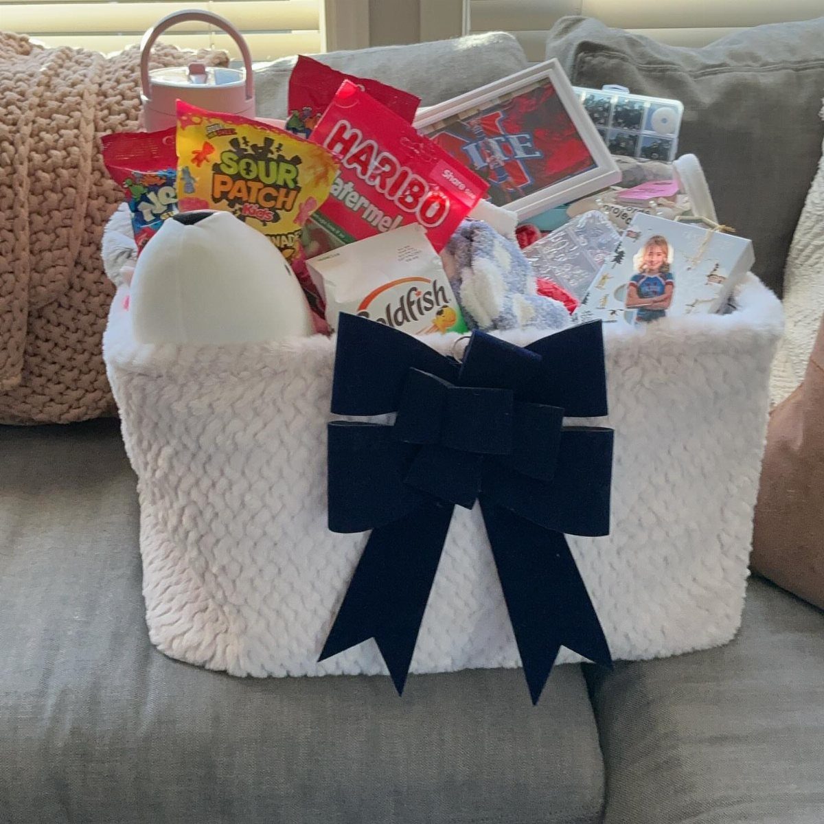 White fuzzy gift basket with navy bow filled with candy and a mug.