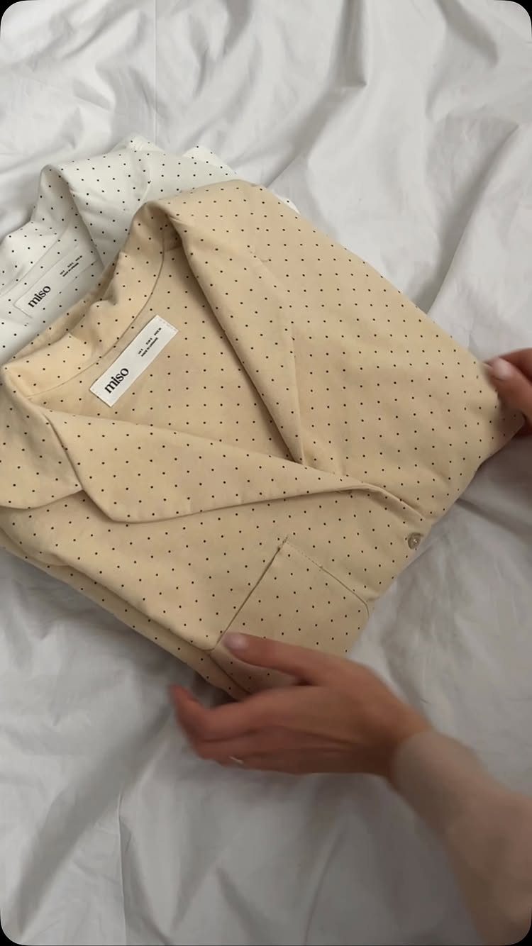 Beige dotted fabric garment held by hands on white wrinkled bed sheets