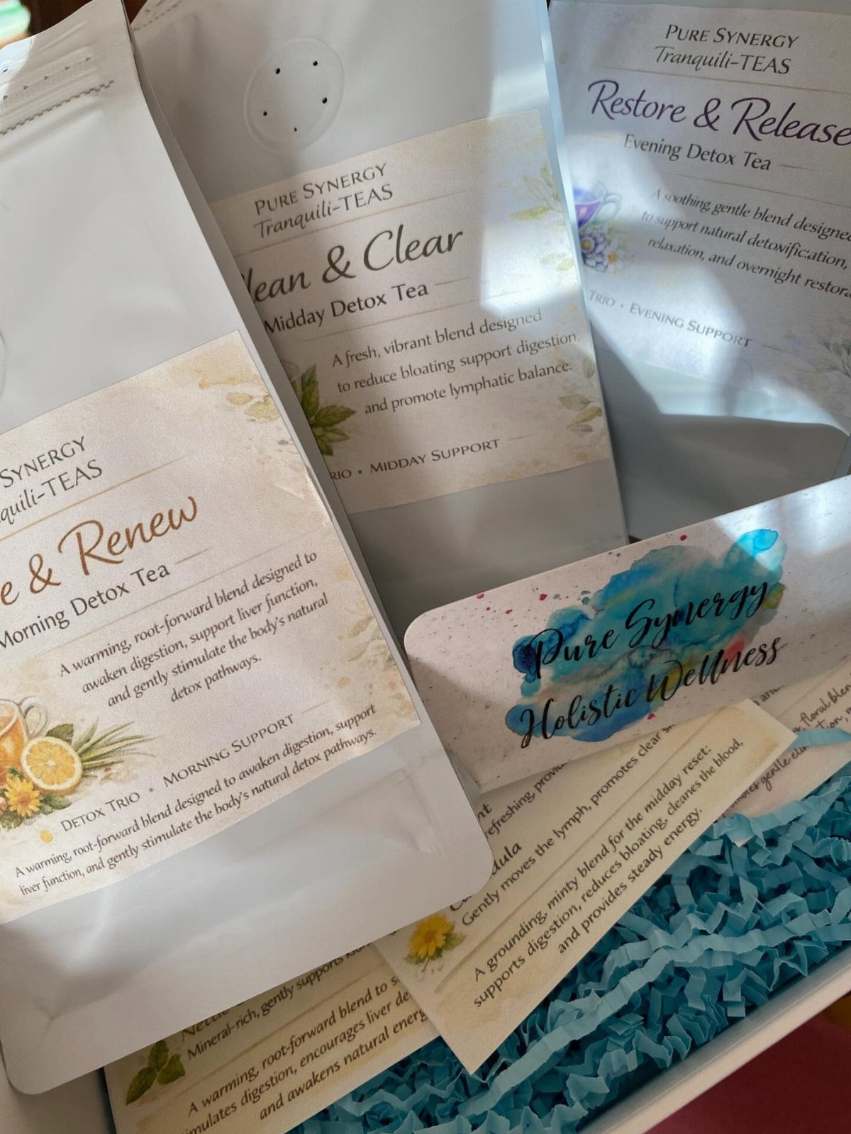 Three white pouches of herbal detox tea in a gift box with blue filler.
