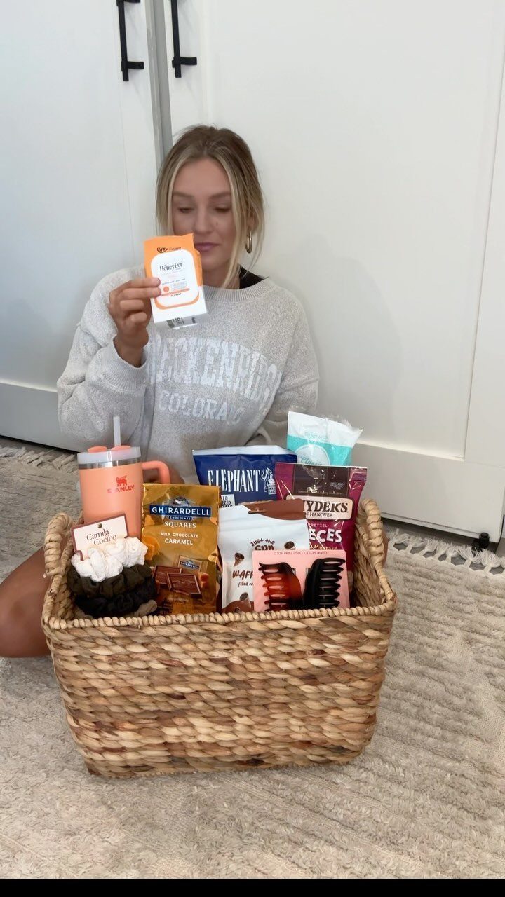 Woman holding a snack packet next to a woven basket of postpartum care items.