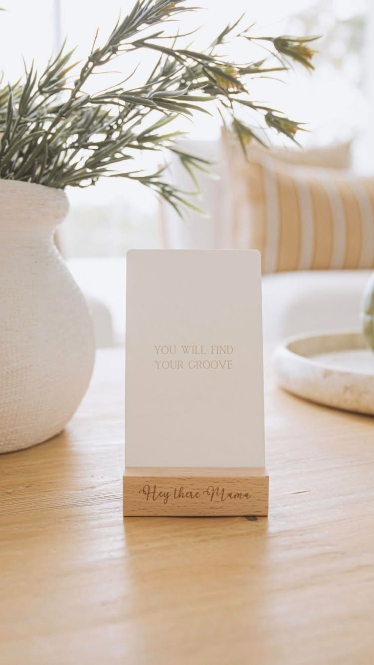 Affirmation card in a wooden holder on a table next to a plant
