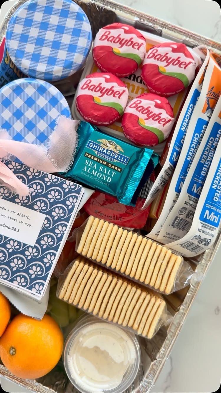 Assorted snacks in a foil tray including cheese, chocolate, crackers, and oranges.