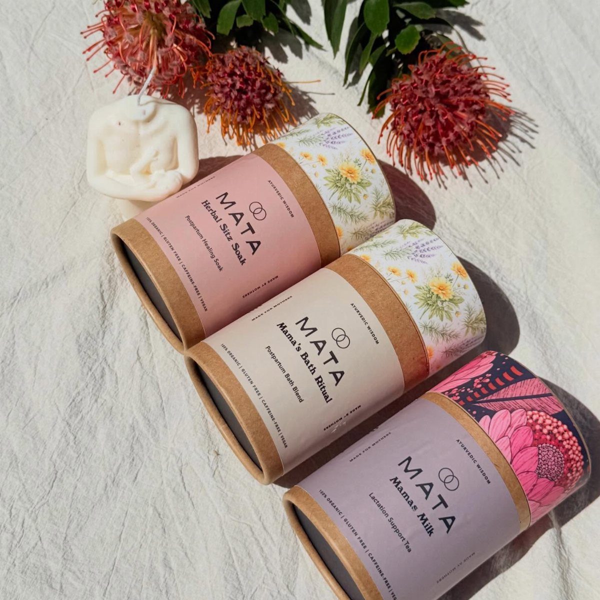Three postpartum care product containers with herbal tea and bath soak on white fabric.