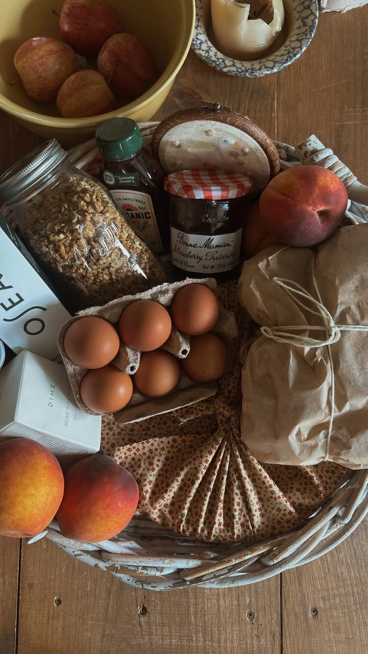 Wicker gift basket containing fresh eggs, peaches, jars of food, and wrapped packages.