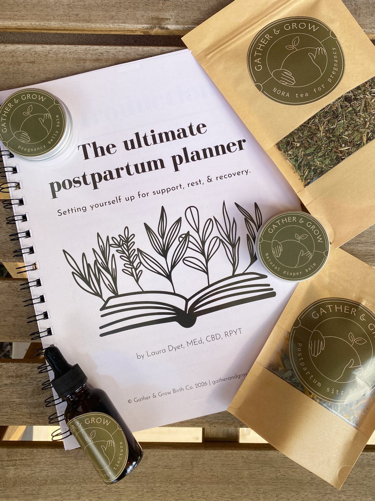 Postpartum planner notebook surrounded by herbal tea pouches and essential oil bottles.