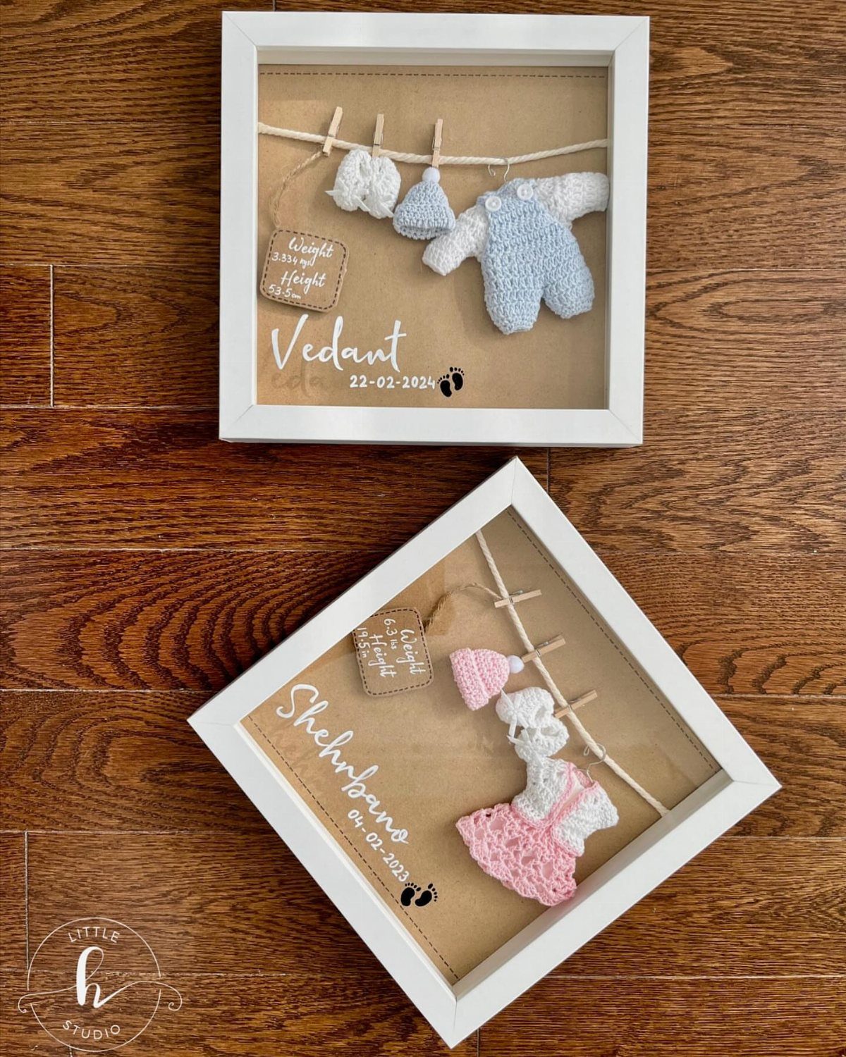 Two white shadow boxes containing crocheted baby clothes and personalized names on glass.