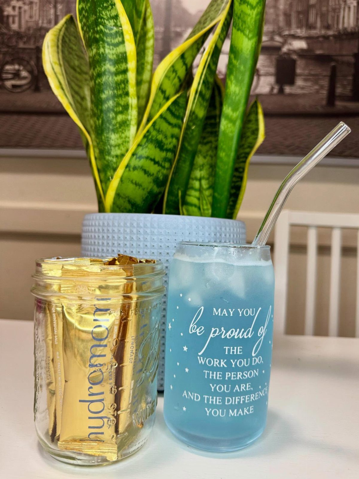 Blue frosted glass with straw and jar of hydration powder packets near plant
