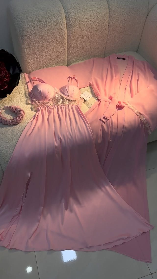 Pink satin nightgown and matching robe set laid on a white sofa.