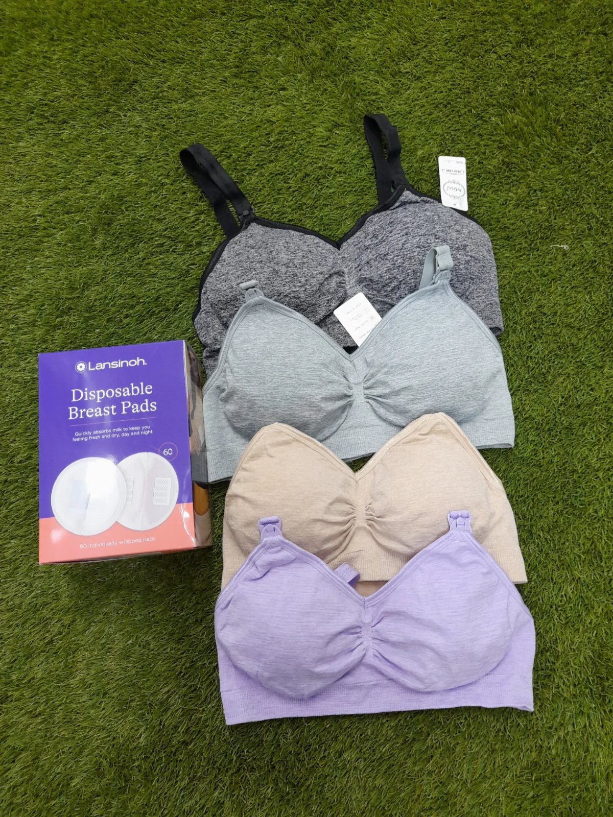 Nursing bras in various colors and a box of disposable breast pads on grass.