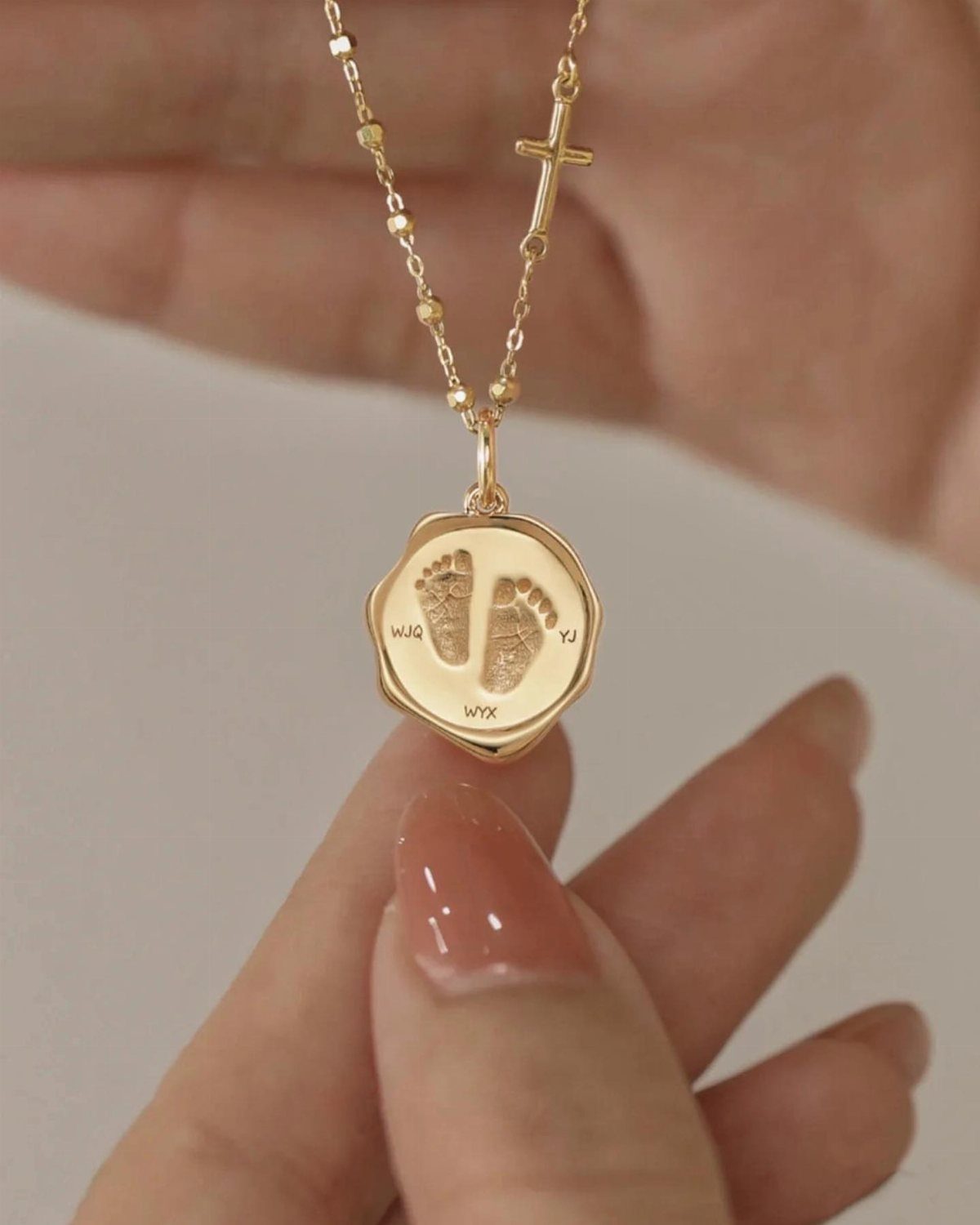 Gold necklace with a circular pendant engraved with baby footprints and initials.