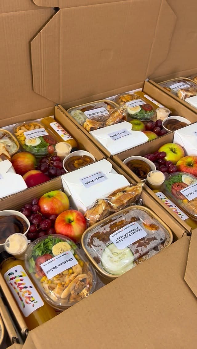 Prepared meal delivery boxes containing fresh salads, fruit, and bottled juice.