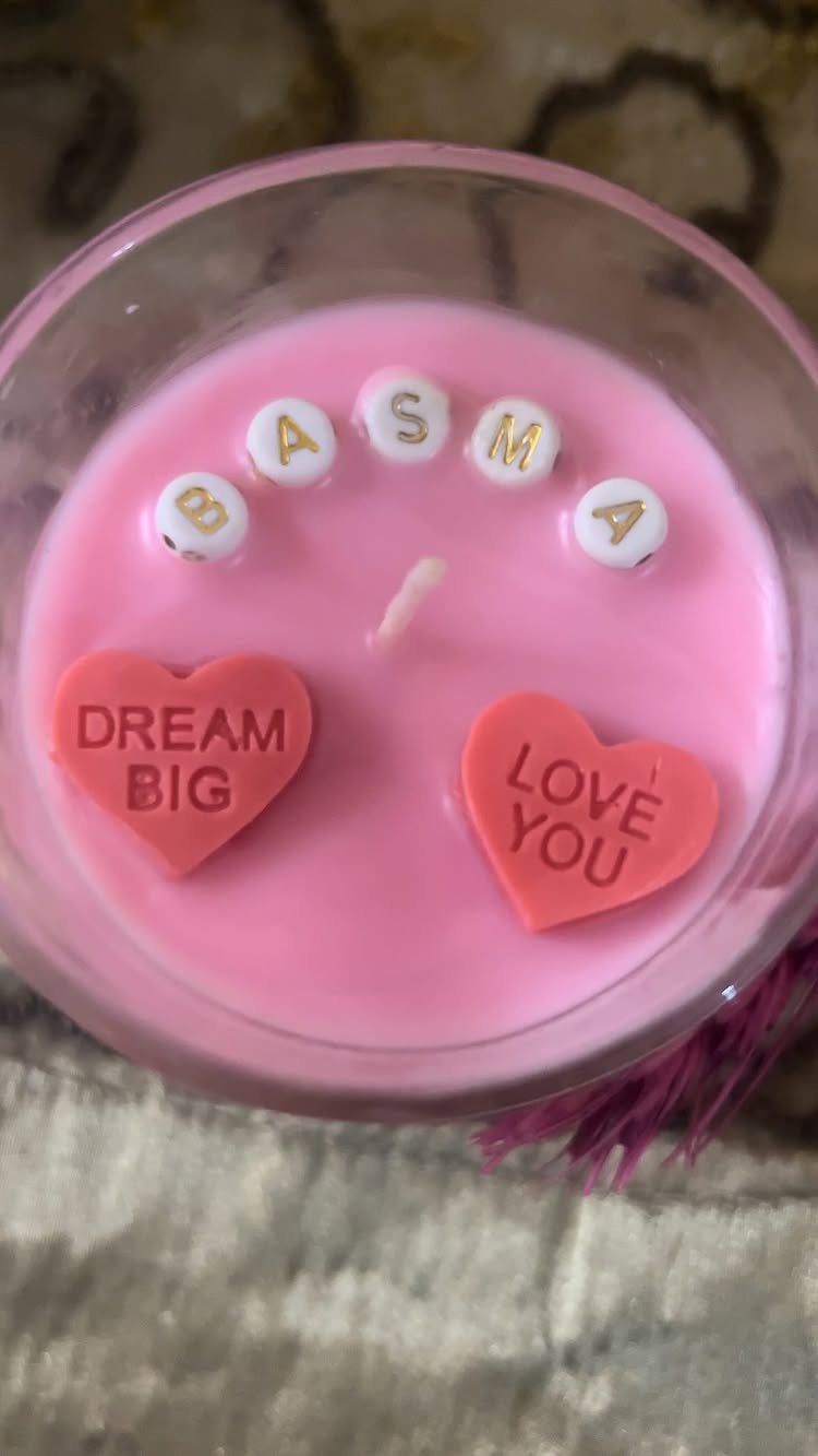 Pink scented candle in a glass jar with personalized beads and heart charms.