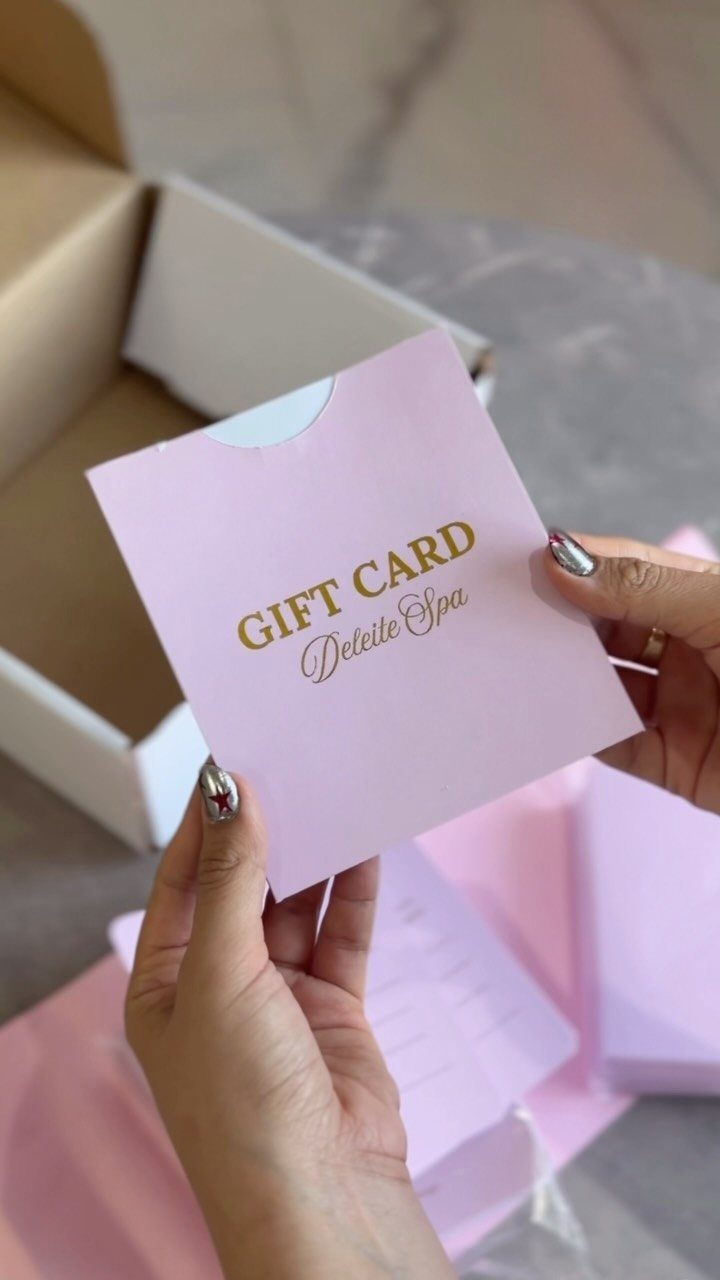 Hands holding a pink spa gift card with gold lettering over a box.