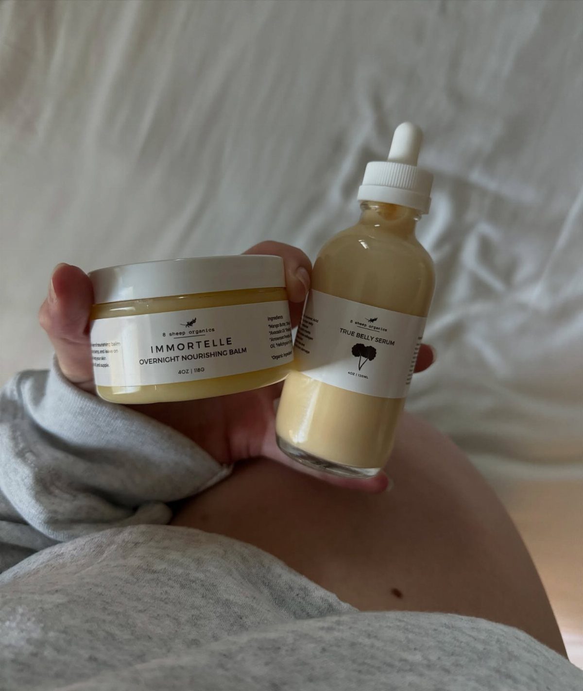 Skincare balm and serum held over a pregnant belly for skin hydration.
