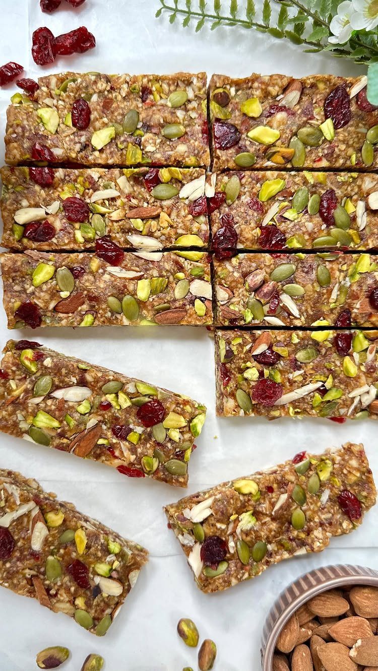 Granola bars topped with nuts and dried berries on white parchment paper.