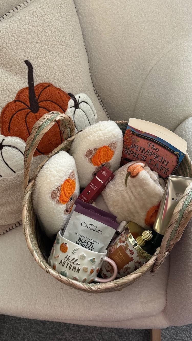 Autumn-themed gift basket with fluffy slippers, a mug, and a book on a chair.
