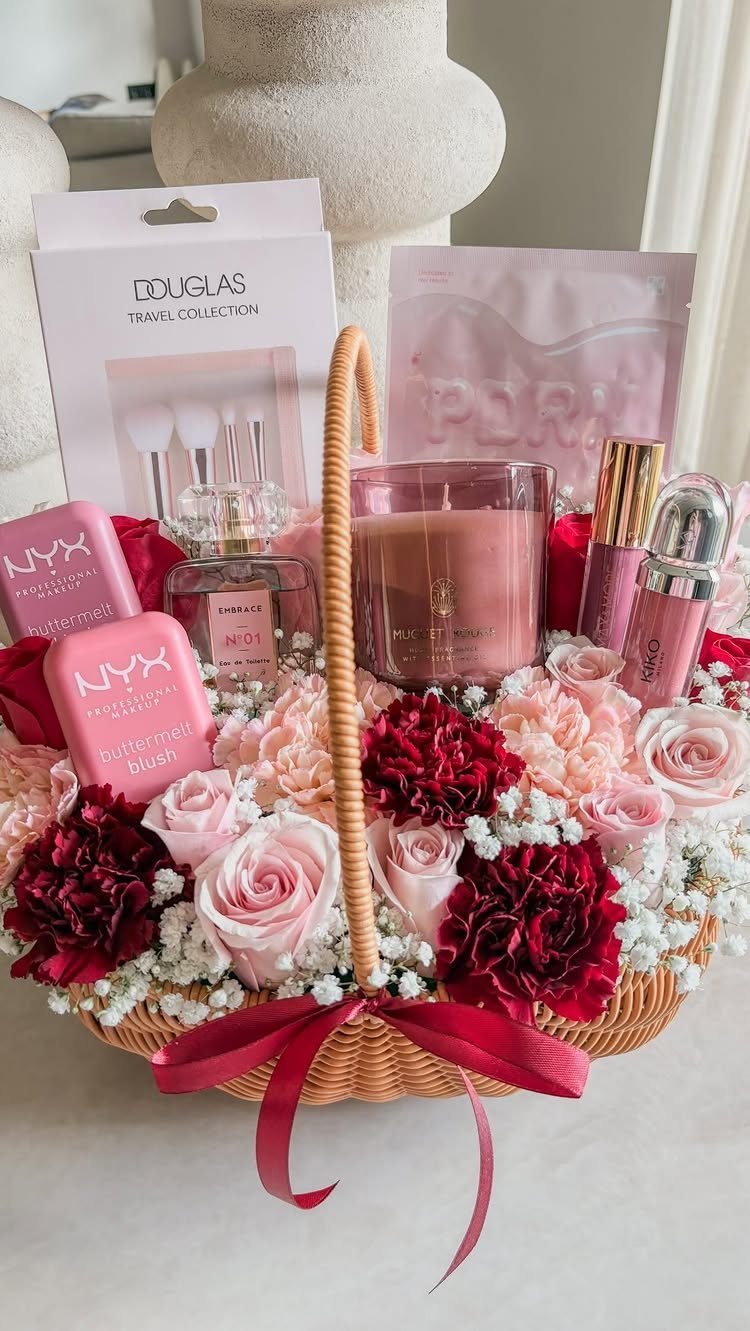Wicker gift basket with pink and red flowers, makeup, perfume, and a candle.