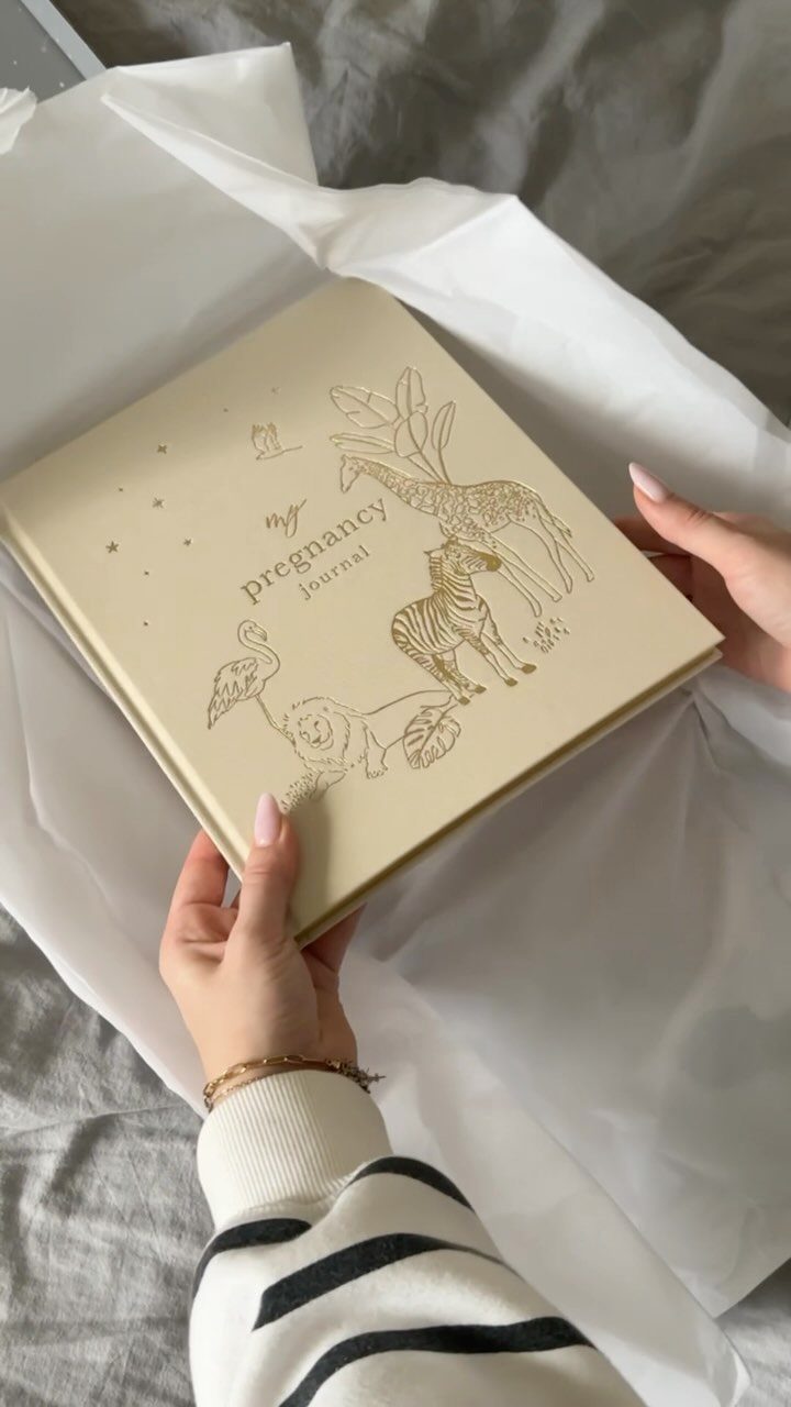 Pregnancy journal with gold animal illustrations held by hands over white tissue paper.