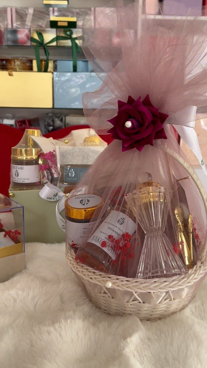 White wicker gift basket with beauty products wrapped in pink tulle and red rose.