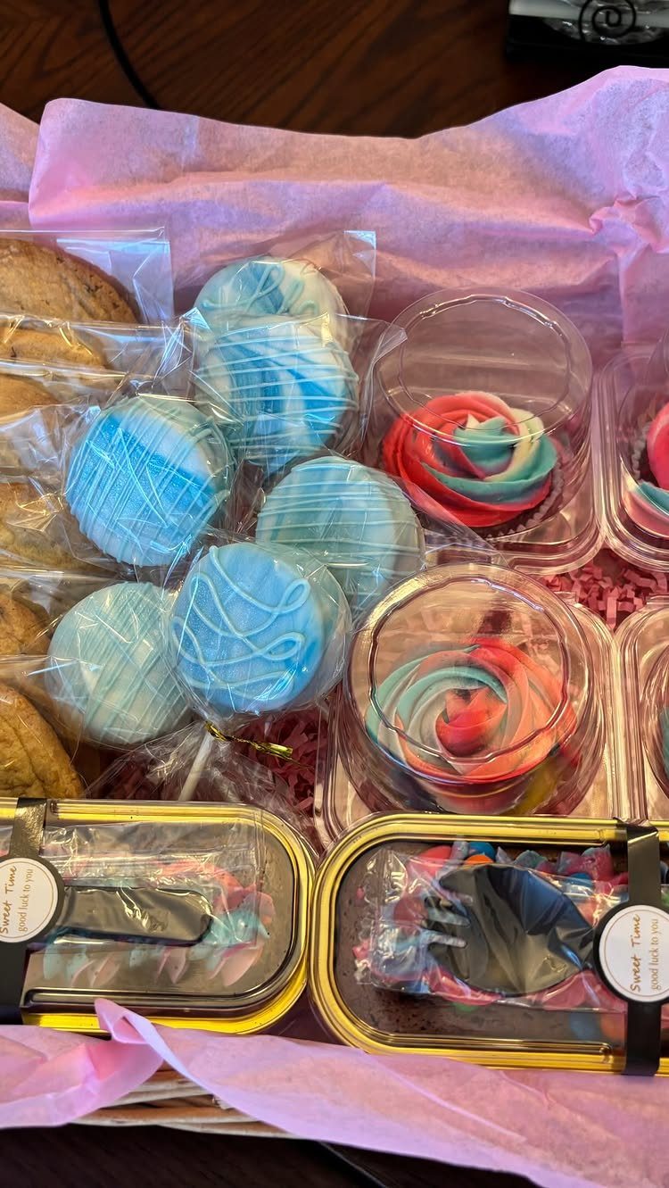 Gift basket filled with blue cake pops, swirl cupcakes, and gold treat tins.