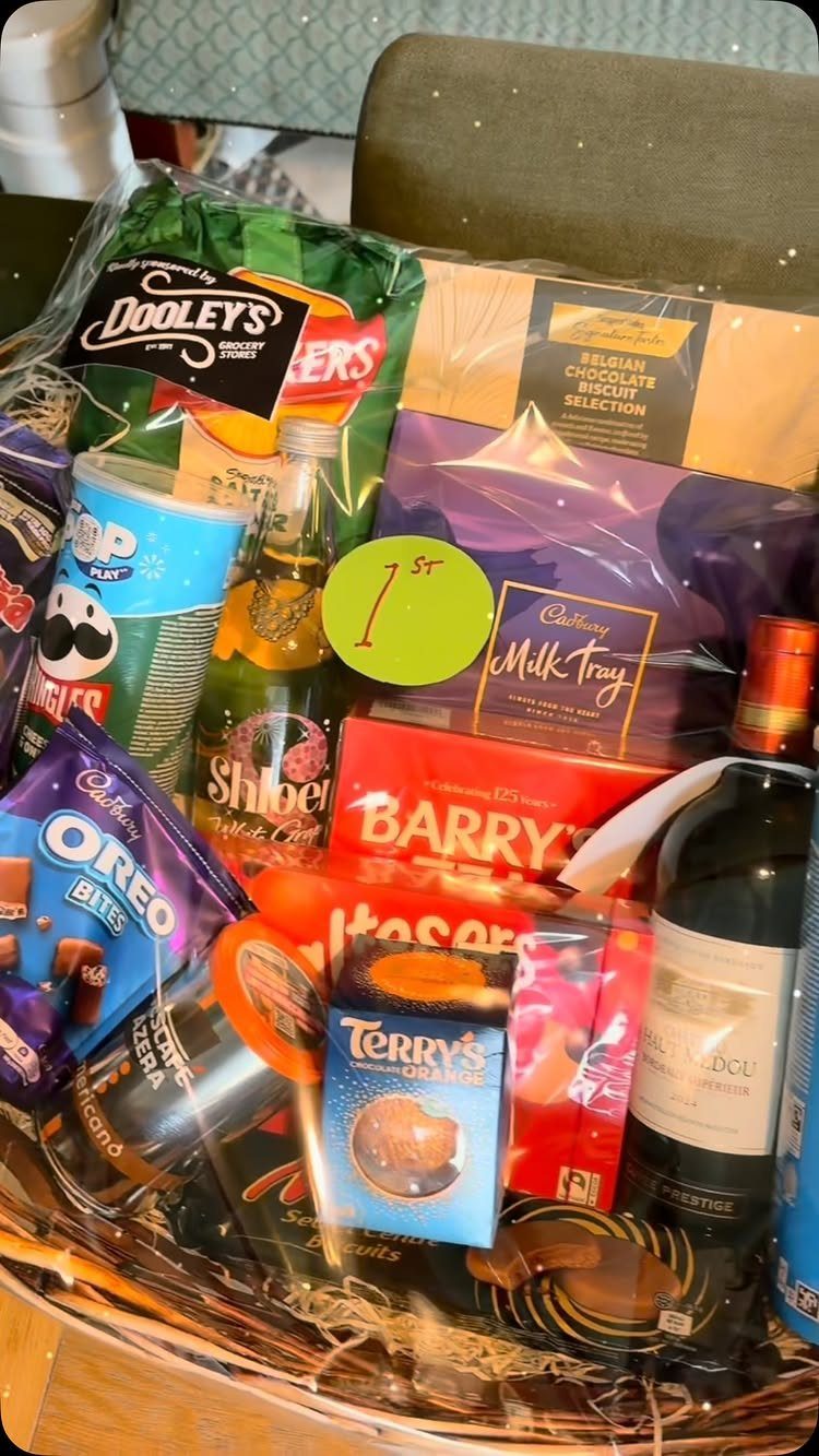 Wicker gift basket filled with assorted chocolates, sweets, and wine wrapped in cellophane.