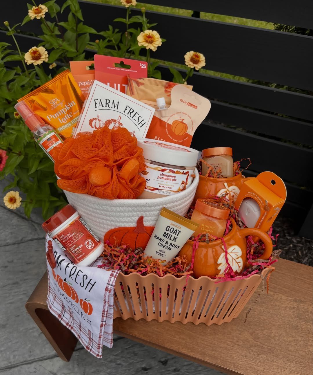 Autumn-themed gift basket with pumpkin products and orange decor on a wooden bench.