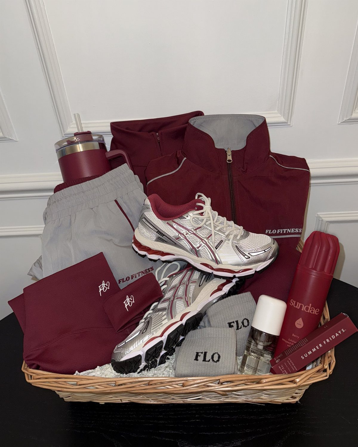 Fitness gift basket with athletic shoes, maroon workout clothes, and a foam roller.