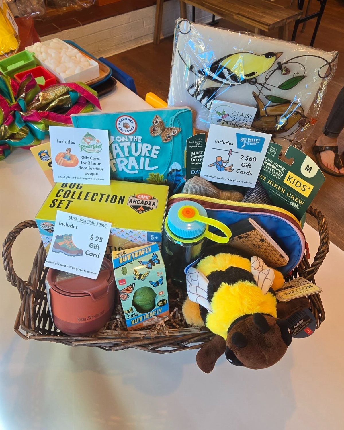 Wicker basket filled with nature exploration kits, gift cards, and a plush bee.