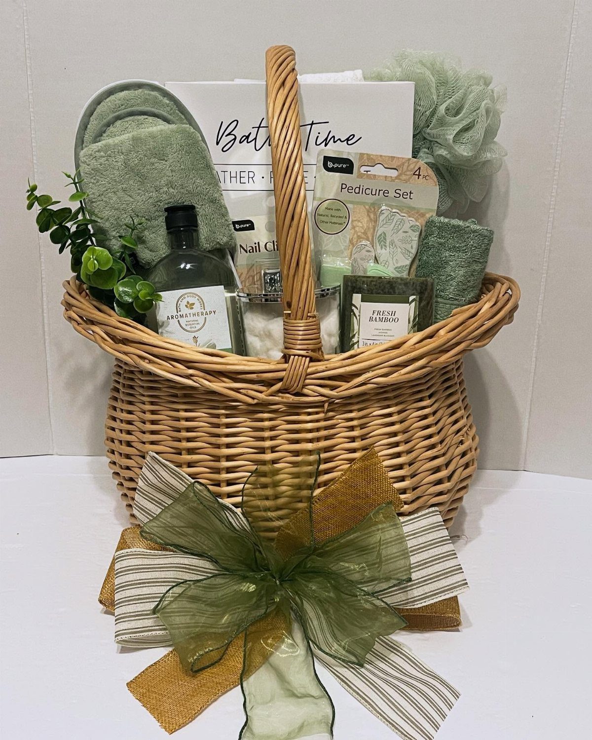 Wicker gift basket filled with green spa products and a large decorative bow.