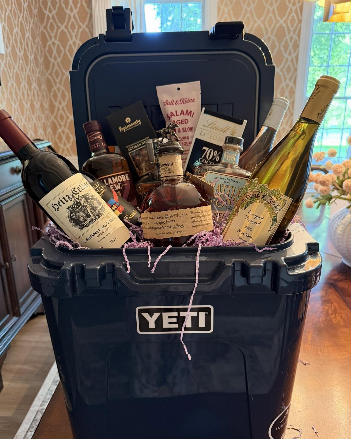 Navy blue Yeti cooler filled with wine, liquor, salami, and chocolate treats.