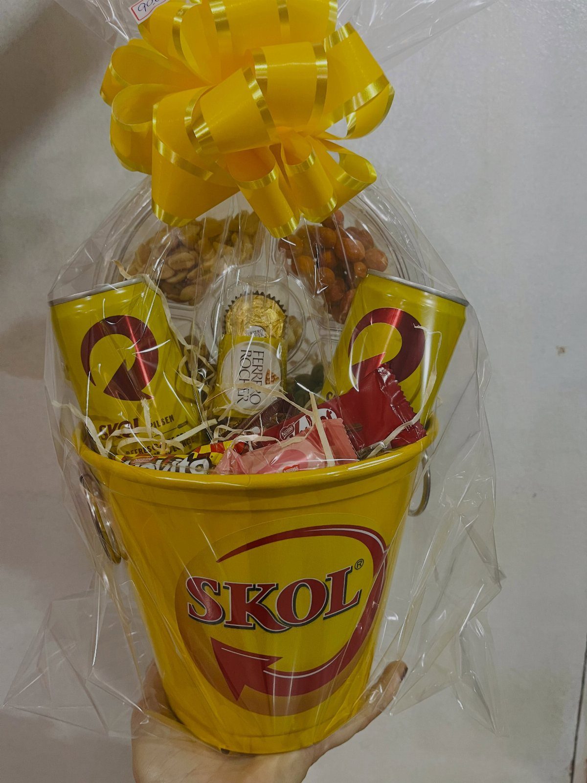 Yellow Skol beer bucket gift basket with cans and snacks wrapped in cellophane.