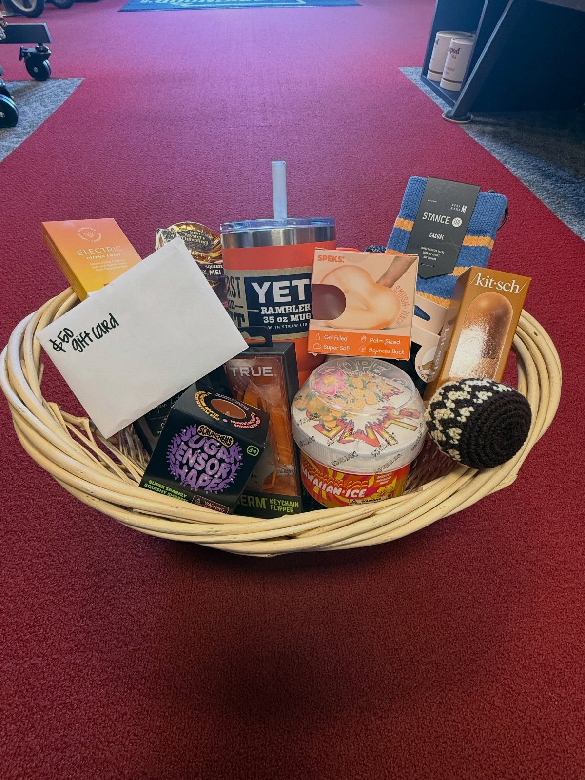 Wicker gift basket filled with a Yeti tumbler, skincare products, and a gift card.