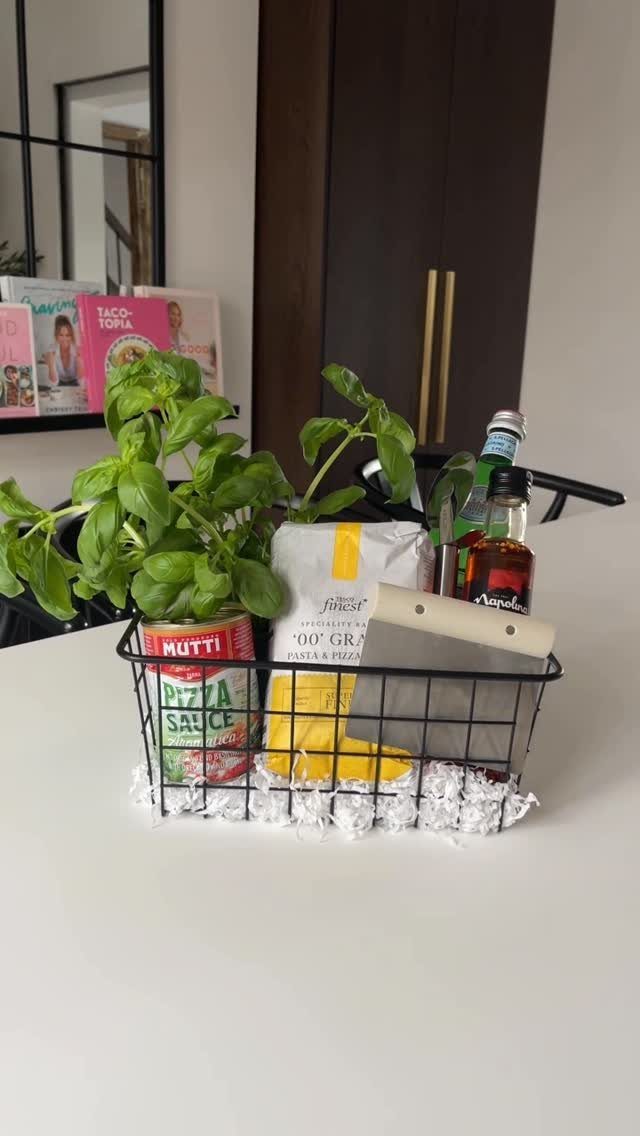 Pizza making kit in a black wire basket with basil, sauce, and flour.