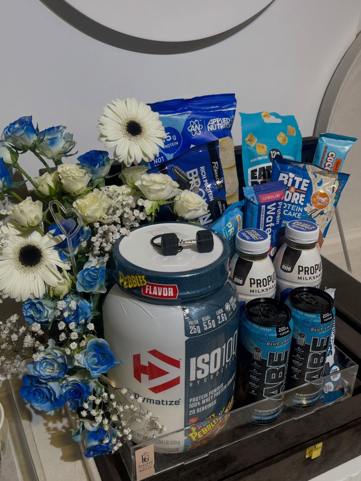 Fitness gift basket with protein powder, shakes, and blue and white flowers.