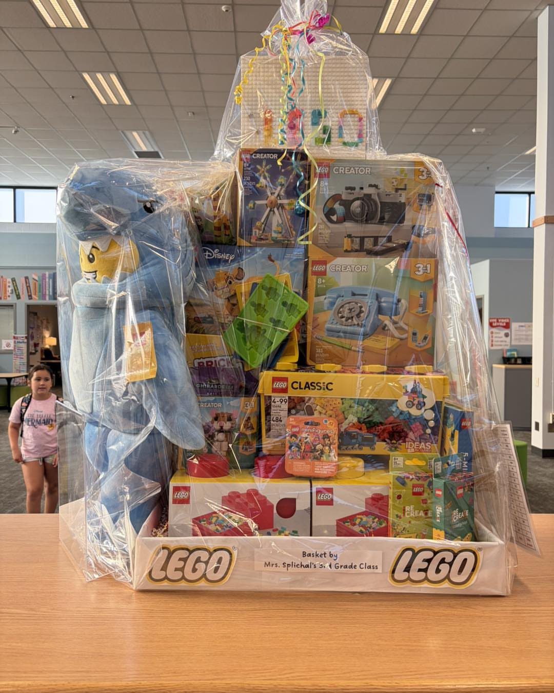 LEGO gift basket with multiple building sets and a blue plush character wrapped in cellophane.