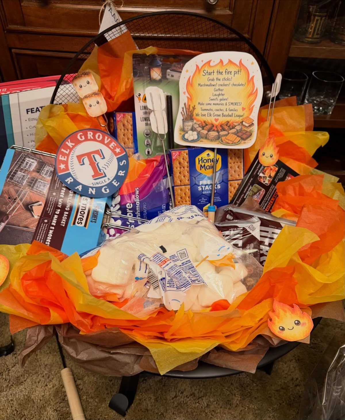 S'mores gift basket arranged inside a black metal fire pit with orange tissue paper.