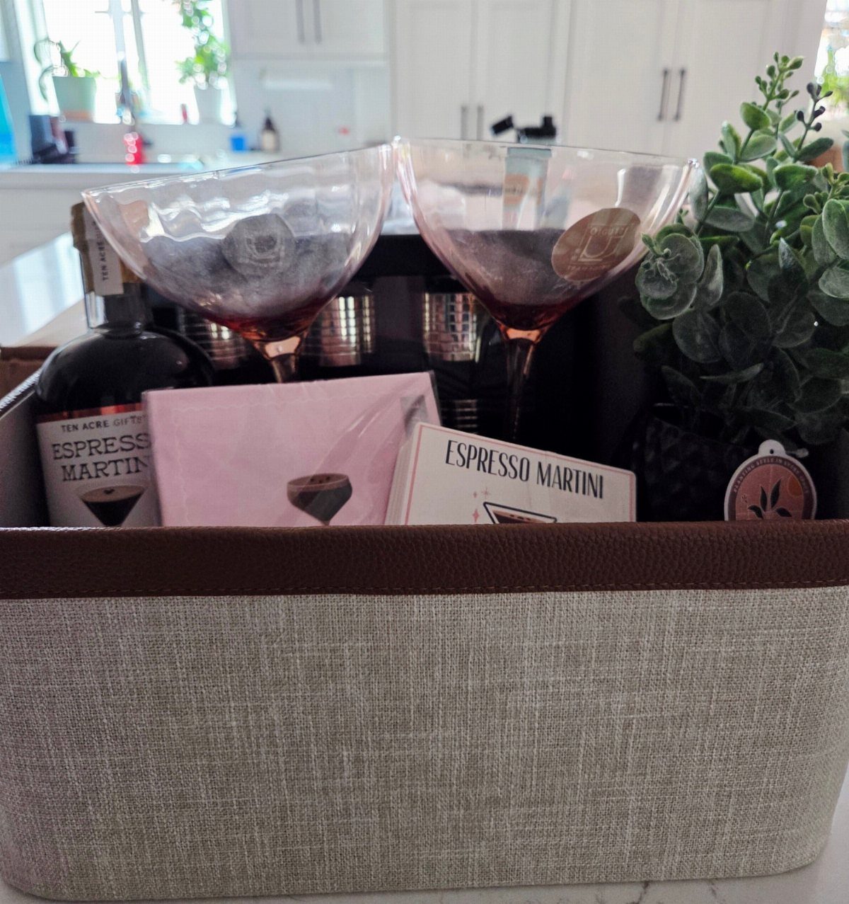 Gift basket with espresso martini liqueur, two martini glasses, and a small plant.